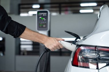 Genç adam EV elektrikli arabasıyla alışveriş merkezinin otoparkına gidiyor şehir merkezindeki şarj oluyor yeşil, temiz, yeniden şarj edilebilir elektrikli araç iç organları ile kentsel sürdürülebilirlik yaşam tarzını gösteriyor