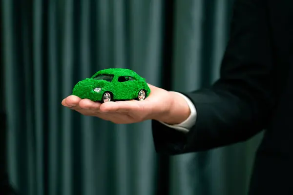 Businessman holding green eco car model. Electric vehicle utilized by eco-friendly business for environmental friendly transportation. Corporate responsible with zero CO2 emission. Quaint