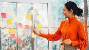 İş adamları ofisteki proje planlama kurulunda çalışıyor ve proje gelişimini analiz etmek için iş arkadaşlarıyla sohbet ediyorlar. Düzenli olması için cama yapıştırılmış yapışkan notlar kullanıyorlar. Jivy