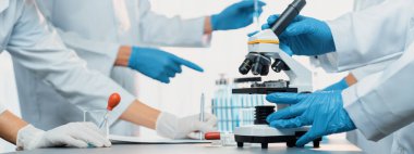 Kendini adamış bir grup bilim adamı yeni bir aşı ilacı ya da antibiyotik geliştirmek için tıbbi laboratuvarda mikroskop kullanarak kimyasal deney yapıyorlar. Biyoteknoloji laboratuvarı ve tıp araştırma konsepti. Neoterik