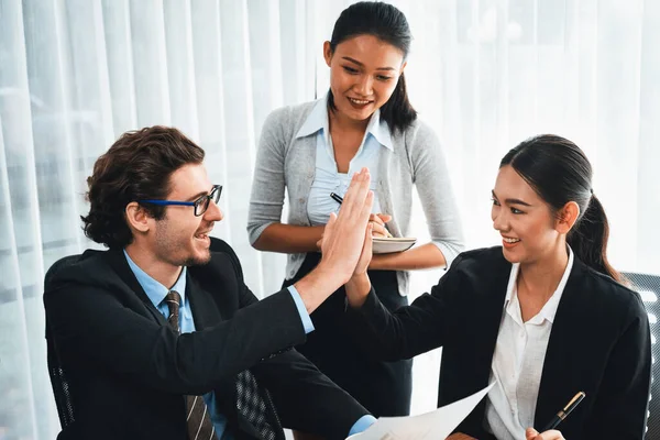 Group of happy businesspeople in high five gesture and successful efficient teamwork. Diverse race office worker celebrate after made progress on marketing planning in corporate office. Meticulous