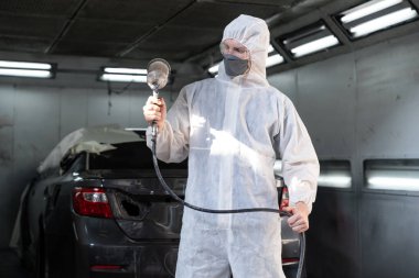 Tam korumalı ekipmanlı otomotiv işçisi sprey tabanca ya da oda atölyesindeki solunum cihazı boyasıyla araba kaportasına ustalıkla renk boyası uygular. Tamir için araba boyama servisi. Oxus.