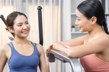 Enerjik ve güçlü atletik Asyalı kadın evde spor arkadaşı ya da antrenörü ile birlikte eliptik koşu makinesiyle koşuyor. Formda fiziğin takibi ve sağlıklı yaşam tarzına bağlılık. Kuvvetli