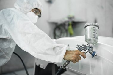Tam korumalı ekipmanlı otomotiv işçisi sprey tabanca ya da oda atölyesindeki solunum cihazı boyasıyla araba kaportasına ustalıkla renk boyası uygular. Tamir için araba boyama servisi. Oxus.