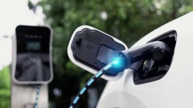 Elektrikli araba, doğal parktaki temiz enerji şarj istasyonundan gelen fütürist akıllı EV şarj cihazının dijital batarya durumu hologramıyla şarj oluyor. Gelecekçi çevre dostu EV araba. İnceleyin