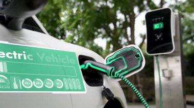 Elektrikli araba, doğal parktaki temiz enerji şarj istasyonundan gelen fütürist akıllı EV şarj cihazının dijital batarya durumu hologramıyla şarj oluyor. Gelecekçi çevre dostu EV araba. İnceleyin