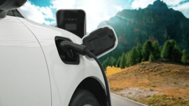 Elektro jeneratör sürücüsüyle enerji sürdürülebilir araba gücü, şarj istasyonunda şarj edilen batarya, ilerici seyahat konsepti için dağ zeminine sahip. Temiz ortamın sembolü olarak doğadaki EV otomobil.