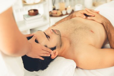 Beyaz adam stres önleyici kafa masajından ve lüks bir tatil beldesi veya otel spa salonundaki modern ışık ortamında yüz güzelliği eğlencelerini şımartmaktan hoşlanıyor. Sessiz.