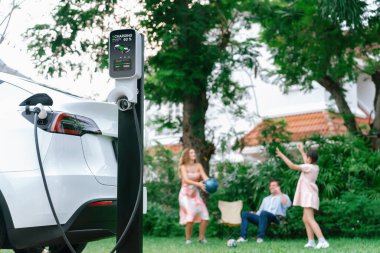 Evde şarj edilen elektrikli araba şarjını mutlu ve neşeli bir ailenin arka planına odakla. EV arabası daha iyi bir gelecek için alternatif ve sürdürülebilir enerji kullanıyor.