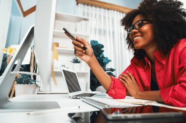 Genç Afrikalı iş kadını projesini ekran monitörü laptopuna odaklıyor, web sitesi bilgisayarındaki veri merkezini ve akıllı telefonu araştırıyor. Mekan teması sade renkte rahat bir odada çalışır. Tatlandırıcı.