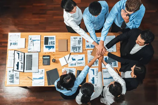 Panorama top view multiracial business people make synergy hand stack together over table with financial paper as analyst team building collaboration for corporate employee in workplace.Meticulous