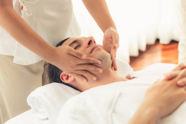 Beyaz adam stres önleyici kafa masajından ve lüks bir tatil beldesi veya otel spa salonundaki modern ışık ortamında yüz güzelliği eğlencelerini şımartmaktan hoşlanıyor. Sessiz.