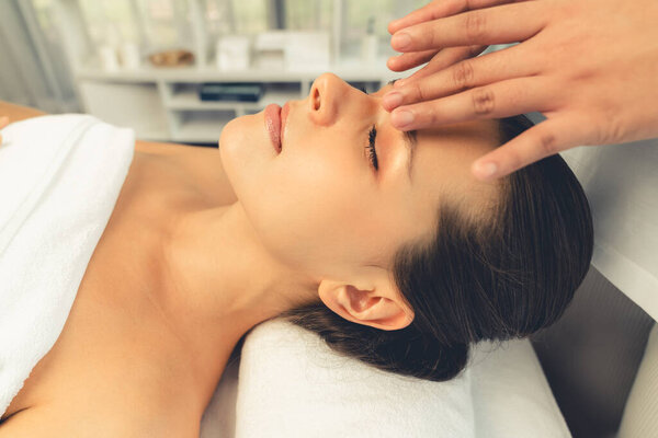 Кавказская женщина наслаждается расслабляющим антистрессовым массажем головы и расслабляющим отдыхом на коже лица в дневном спа-салоне современного света в роскошном курорте или спа-салоне отеля. Quiescent