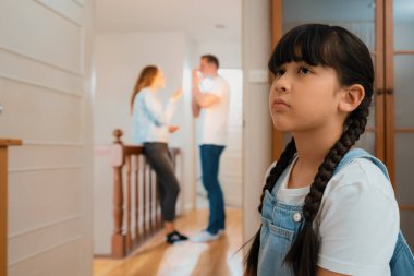 Stresli ve mutsuz genç kız arka planda ebeveynleri tartışırken köşede ağlayıp üzülüyor. Evde aile içi şiddet ve travmatik çocukluk depresyona dönüşür. Eşzamanlama