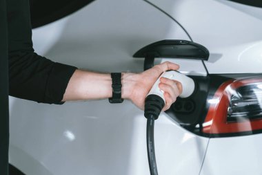 Genç adam EV elektrikli arabasıyla alışveriş merkezinin otoparkına gidiyor şehir merkezindeki şarj oluyor yeşil, temiz, yeniden şarj edilebilir elektrikli araç iç organları ile kentsel sürdürülebilirlik yaşam tarzını gösteriyor
