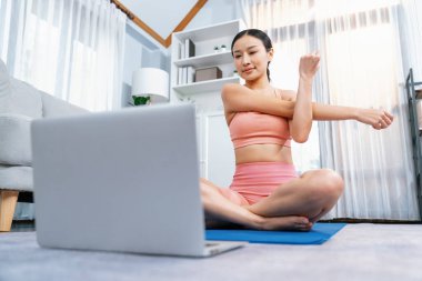 Spor kıyafetli Asyalı bir kadın spor salonunda antrenman yaparken spor minderinde yoga yapıyor. Sağlıklı vücut bakımı kadın dizüstü bilgisayardan yoga videosu izliyor. Kuvvetli