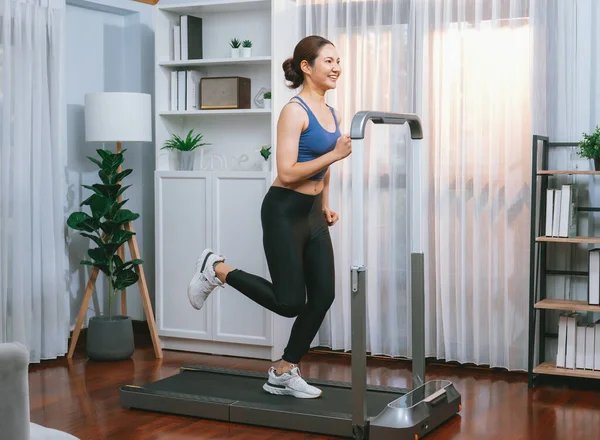 Enerjik ve güçlü atletik Asyalı kadın evde koşu makinası çalıştırıyor. Formda fiziğin takibi ve ev çalışması ve eğitimle sağlıklı yaşam tarzına bağlılık. Kuvvetli