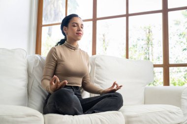 Genç Afrikalı Amerikalı kadın, zihinsel sağlık gücünü ve huzur dolu güzel yaşamı geliştirmek için ev oturma odasında çok dikkatli meditasyon yapıyor.