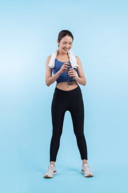 Atletik ve sportif Asyalı kadın yoğun kardiyo antrenmanından sonra dinleniyor ve su içiyor. Stüdyoda sağlıklı egzersiz ve vücut bakımına uygun yaşam tarzı takibi izole edilmiş bir arka plan. Kuvvetli