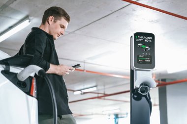 Genç adam EV elektrikli arabasıyla alışveriş merkezinin otoparkına gidiyor şehir merkezindeki şarj oluyor yeşil, temiz, yeniden şarj edilebilir elektrikli araç iç organları ile kentsel sürdürülebilirlik yaşam tarzını gösteriyor