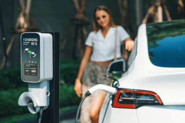 Genç bir kadın yazın yeşil sürdürülebilir şehir bahçesinde EV elektrikli arabasıyla seyahat ediyor. Kentsel sürdürülebilirlik yaşam tarzı yeşil temiz yeniden şarj edilebilir enerji elektrikli BEV araç iç organları