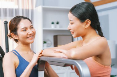 Enerjik ve güçlü atletik Asyalı kadın evde spor arkadaşı ya da antrenörü ile birlikte eliptik koşu makinesiyle koşuyor. Formda fiziğin takibi ve sağlıklı yaşam tarzına bağlılık. Kuvvetli