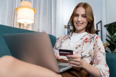 Genç mutlu kadın internetten alışveriş yaparak ürün satın alırken aynı zamanda internet üzerinden online ödeme sistemi ile çevrimiçi mağaza platformundan en yüksek siber güvenlik tarafından korunan ürünler sipariş ediyor.
