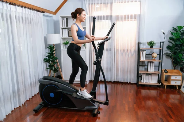 Enerjik ve güçlü atletik Asyalı kadın evde eliptik koşu makinesiyle koşuyor. Formda fiziğin takibi ve ev çalışması ve eğitimle sağlıklı yaşam tarzına bağlılık. Kuvvetli