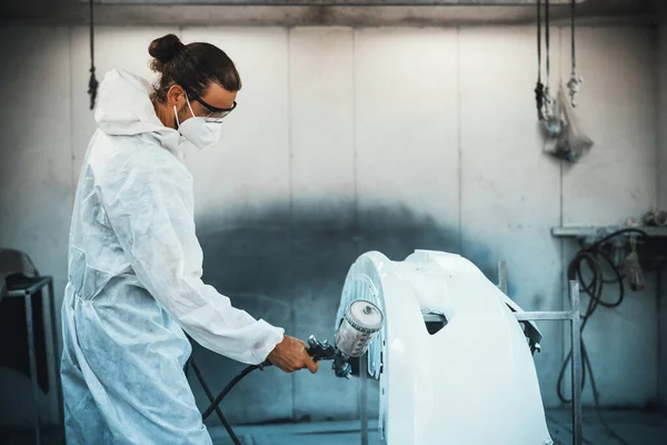 Automotive service worker in protective gear expertly applying color paint in to cars bodywork with spray gun or respirator painting in chamber workshop. Car paint service for scratch refinish. Oxus