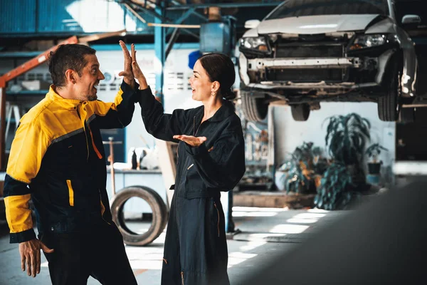 Two happy vehicle mechanic celebrate and high five after made successful car inspection or repair in automotive service car workshop. Technician team enjoy accomplishment together in garage. Oxus
