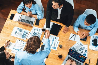 Toplantı odasında iş arkadaşıyla tokalaşan iki işadamı neşeli bir alkış veriyor. Analistlerden oluşan ekip, iş stratejik performansında kaydedilen önemli ilerlemeyi kutluyor. Çok titiz.