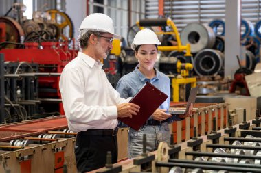 Metal imalatında makine mühendisliği denetleyicisi olarak liderlik örneğini sunan çelik endüstriyel makineyi incelemek için dizüstü bilgisayar kullanan fabrika mühendisi ve asistan..