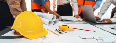 Mühendislik aracı, mimari tasarım tasarımı ve miğfer miğferi bulanık mühendis ve mimarın arka planda çalıştığı ve tartıştığı müteahhitlerin kağıt projesiyle toplantı masasında. İçgörü