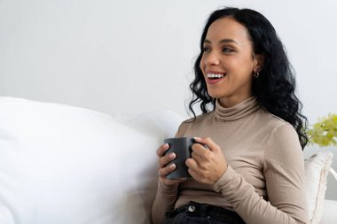 Evdeki kanepede kahve içen mutlu kadın dinlenmek ve dinlenmek için çok önemli. Elinde fincanla genç bir Afrikalı Amerikalı kadının portresi..