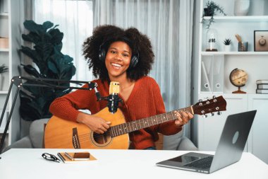 Genç Afrikalı Amerikalı müzisyenin sunucu kanalı gitar çalıyor, şarkı söylüyor, stüdyoda dizüstü bilgisayardan yayın yapıyor. Kulaklık dekorasyonu ve mikrofon kaydı. Tatlandırıcı.