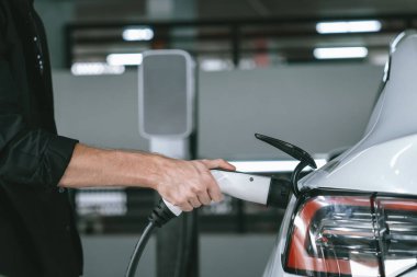 Genç adam EV elektrikli arabasıyla alışveriş merkezinin otoparkına gidiyor şehir merkezindeki şarj oluyor yeşil, temiz, yeniden şarj edilebilir elektrikli araç iç organları ile kentsel sürdürülebilirlik yaşam tarzını gösteriyor