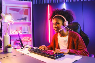 Neon renkli aydınlatma odasında kulaklık takan Afrika kökenli Amerikalı kız flamalı Esport yetenekli takımıyla online dövüş yapıyor. Rakiplerini kazanmak için strateji planlayan diğer oyuncularla konuşmak. Tatlandırıcı.
