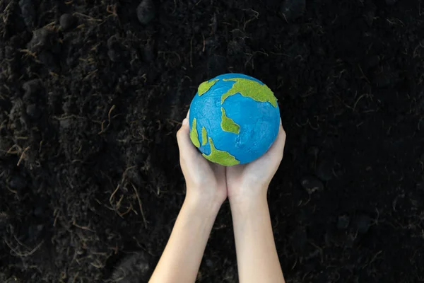 Young boys hand holding planet Earth globe on fertile soil background as Earth day to save this planet with ESG principle and environment friendly energy for brighter future. Gyre