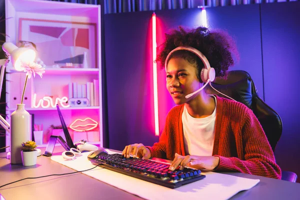 African American girl streamer playing online fighting with Esport skilled team wearing headphones in neon color lighting room. Talking other players planing strategies to win competitors. Tastemaker.