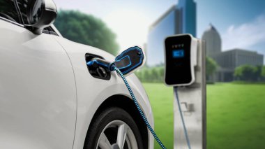EV şarj kablosu ile elektrik yüklemek için elektrik istasyonuna eko yeşil şehir parkındaki elektrik kablosu takıldı. Geleceğin yenilikçi EV arabası alternatif temiz enerji kullanarak CO2 'yi azaltıyor. İnceleyin