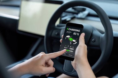 Çevre dostu araba konseptiyle tatil gezisi. Sürücü koltuğunda oturan çevre bilinci olan kadın araba yolculuğu sırasında akü durumunu akıllı telefondan kontrol ediyor. Kalıcı