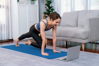 Spor kıyafetli Asyalı bir kadın antrenman rutini olarak spor minderinin üzerinde burpee yapıyor. Çekici kız sağlıklı yaşam tarzını online egzersiz videosuyla takip ediyor. Kuvvetli