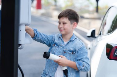 Küçük çocuk EV şarj istasyonundan çevre dostu elektrikli araba şarj ediyor. Temiz, yenilenebilir ve sürdürülebilir enerjiyle çalışan alternatif ulaşım için EV araba yolculuğu konsepti. Kalıcı