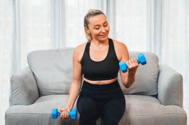 Sportif ve sportif yaşlı kadın vücut egzersizi yapıyor, kanepede oturuyor ve evde dambılı kaldırıyor emeklilikten sonra vücut ağırlığına uygun sağlıklı vücut konsepti olarak. Etki