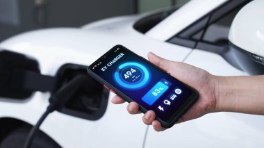 Akıllı telefon ekranı akıllı EV mobil uygulama üzerinde pil durumu EV araba garajdaki ev şarj istasyonu ile elektrik şarj ederken. Geleceğin yenilikçi EV arabası ve enerji sürdürülebilirliği. İnceleyin