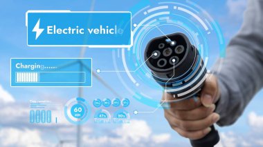 Kameranın önüne odaklanmış EV şarj cihazı bulanık iş adamlarının el rüzgar türbini çiftliği ile batarya durum hologramını gösteriyor. Karbondioksit salınımını azaltmak için temiz enerji kullanan elektrikli araba şarjı tıpası.