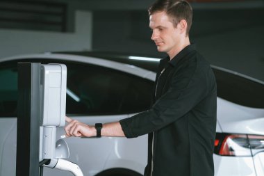 Genç adam EV elektrikli arabasıyla alışveriş merkezinin otoparkına gidiyor şehir merkezindeki şarj oluyor yeşil, temiz, yeniden şarj edilebilir elektrikli araç iç organları ile kentsel sürdürülebilirlik yaşam tarzını gösteriyor