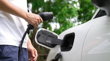 İlerici adam elektrikli aracına elektrik kablosu takıyor. Ev şarj istasyonundan EV arabası. Çevreyi korumak için temiz ve yenilenebilir enerji kullanan elektrikli bir araba. Çevre dostu otomobil.