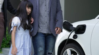 Elektrikli arabası ve şarj istasyonu olan yenilikçi bir genç aile ve kız. Sağlıklı çevre için elektrikli araçlardan gelen yeşil ve temiz enerji. Yenilenebilir kaynaktan eko güç.