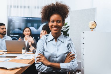 Bir grup ofis çalışanı ile birlikte arka planda ekranda gösterim paneliyle buluşan mutlu Afrikalı genç bir iş kadını portresi. Takım toplantısında kendine güveni tam bir ofis hanımı. Uyum
